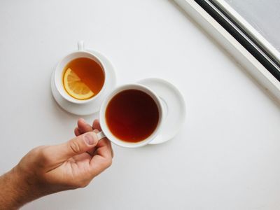 Hands holding a cup of tea near a bright window
